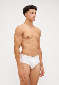 Slip bianco in cotone con vita testurizzata su cui è impresso il logo "GAP". Finitura liscia, vestibilità aderente e design semplice. Il modello è in posizione eretta.