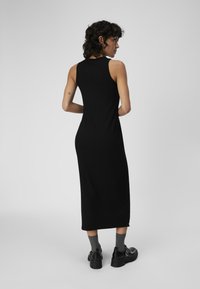 Vestido midi negro, sin mangas, con un diseño ajustado y una textura suave. Se lleva con calcetines grises y zapatos negros de suela gruesa.