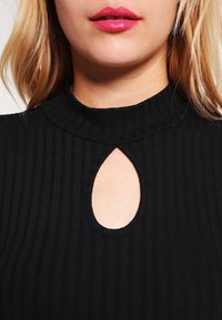 Haut noir côtelé avec un col montant et une petite découpe en goutte d'eau à l'avant. Le tissu est doux avec une finition texturée.