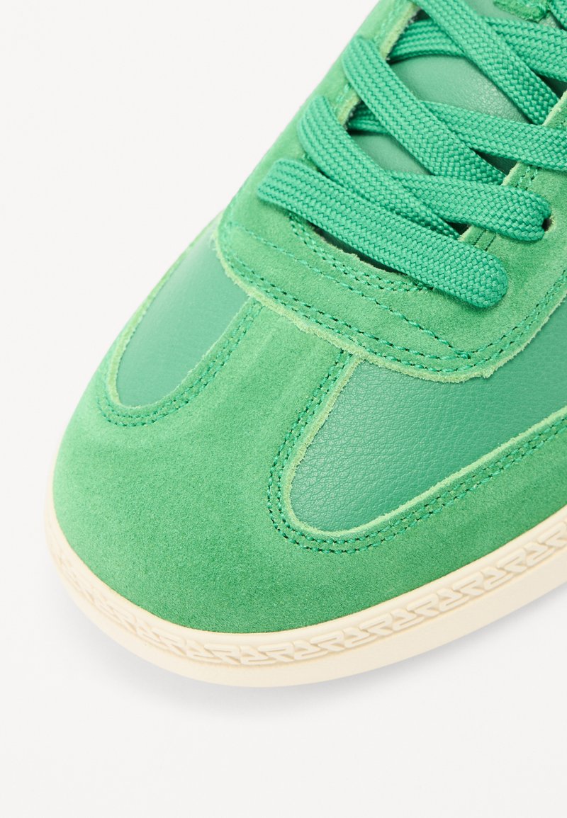 Sneaker verdi con un mix di suede e pelle liscia, lacci testurizzati e una suola in gomma di colore chiaro.