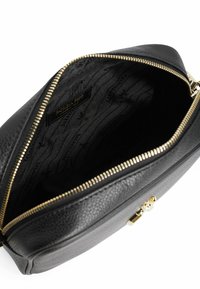 Interno di una borsa in pelle nera con finitura testurizzata, zip dorata e fodera in tessuto nero con marchio caratterizzata da un motivo sottile.