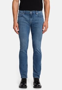 Hellblaue Slim-Fit-Jeans aus Denim mit einem klassischen Fünf-Taschen-Design und dezenten Nähten. Kombiniert mit schwarzen Schuhen.