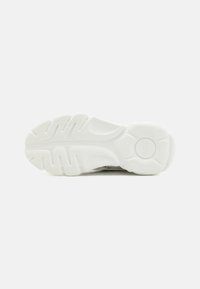 Sole di sneaker bianca con gomma testurizzata e motivo ondulato per la presa, punta arrotondata e dettaglio del logo circolare sul tallone.