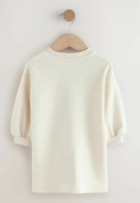 Pullover color crema con collo a costine, maniche a sbuffo 3/4 e motivi maculati in colori pastello. Appeso a una gruccia di legno su uno sfondo chiaro.
