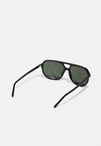 Ochelari de soare negri cu lentile verzi, formă rectangulară, cadru din plastic neted și brațe subțiri cu un branding discret pe o parte.