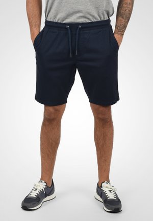 Marineblauwe shorts met elastische tailleband en trekkoord, met zijzakken en een relaxed fit. Draag ze met grijze sport sneakers.