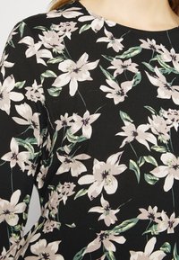 Svart tyg med ett blommönster bestående av stora vita och ljusrosa blommor samt gröna blad, slät textur och rund halsringning.