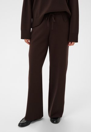 Person wearing dark brown wide-leg pants with drawstring waist and matching long-sleeve top, paired with black flat shoes.