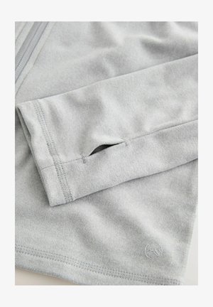 Light gray long-sleeve top with a smooth texture, featuring a small thumb hole in the cuff and subtle logo embroidery.
