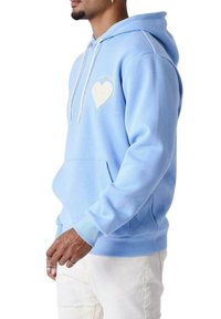 Felpa azzurro chiaro in tessuto morbido, con un design a forma di cuore in materiale lucido, cordini regolabili e tasca frontale tipo kangaroo.