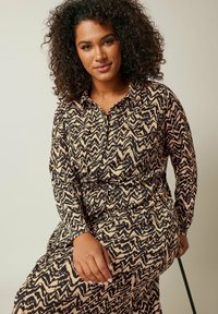 Langärmliges, knöpfbares Kleid mit einem schwarz-beigen Zickzackmuster, aus texturiertem Stoff und mit elastischem Bund für einen figurbetonten Look.