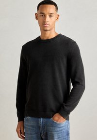 Schwarzer Strickpullover mit Rundhalsausschnitt und Rippbündchen, kombiniert mit hellblauen Jeans. Strukturierter Stoff, figurbetonte Form, lässiges Design.
