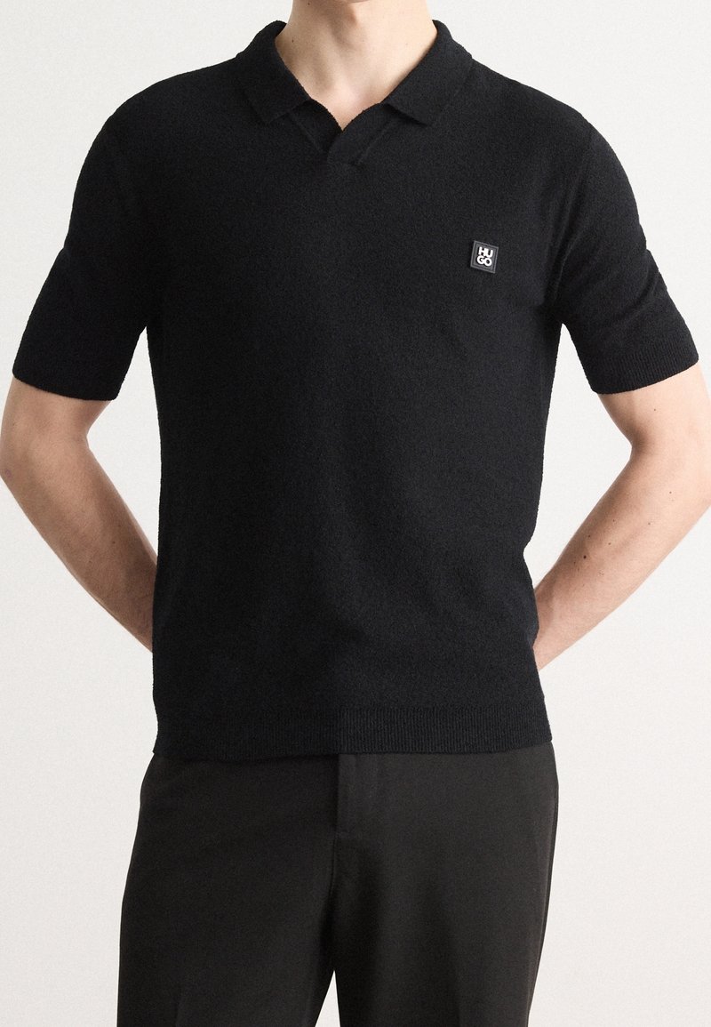 Korte mouwen zwarte polo shirt van gestructureerde stof, met een kraag en een klein merkembleem op de linkerkant van de borst.