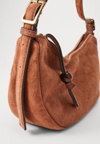 Borsa in suede marrone a forma curva. Presenta una tracolla in pelle con una chiusura dorata e un accento decorativo in legno. Texture liscia.
