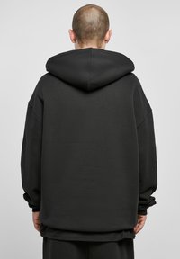 Schwarzer übergroßer Hoodie mit Kordelzugkapuze, überschnittenen Schultern und langen Ärmeln; aus einem glatten, weichen Stoff mit minimalistischem Design.