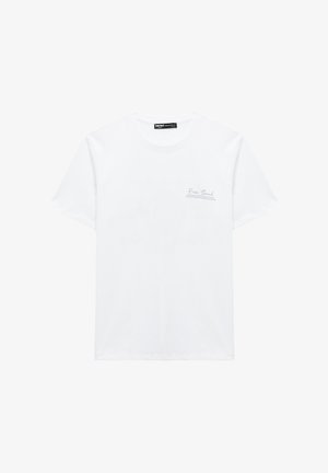 T-shirt blanc en coton à manches courtes avec col rond et petit texte "Free Soul" sur le côté gauche de la poitrine.