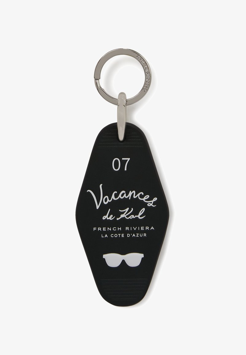 Étiquette de clé en caoutchouc noir avec un anneau en métal argenté, présentant un texte blanc et un graphique de lunettes de soleil, marqué "07" et "Vacances de Karl."