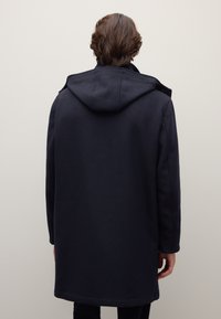 Cappotto in lana blu scuro con cappuccio, caratterizzato da un taglio dritto, maniche lunghe e design minimalista. Nessuna ferramenta o motivo visibile.