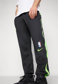 Férfi fekete melegítőnadrág zöld oldalsávokkal, Nike logóval és NBA emblémával. Simító, rugalmas anyagból készült.