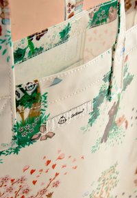 Újrahasználható szatyor krémszínű háttérrel, színes fa-, állat- és virágillusztrációkkal. Logócímke található rajta.