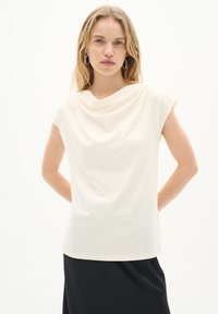 Haut drapé crème avec des manches courtes, fabriqué en tissu doux. Il présente un col rond et une coupe décontractée, associé à une jupe noire.