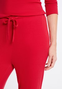 Rood geribd loungewear van stof met een losse pasvorm, voorzien van een trekkoord in de taille en een zachte textuur, met details van het torso en de hand.