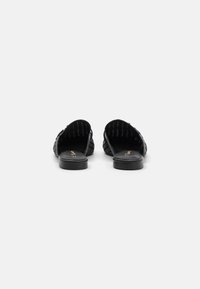 Black woven slip-on shoes with a flat sole, featuring a textured upper and minimalistic design. Interior has a smooth, dark lining.