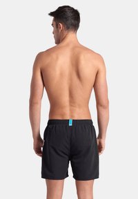 Shorts de baño negros con una cómoda cintura elástica y un detalle azul en la parte trasera. Textura suave y diseño de longitud media hasta el muslo.