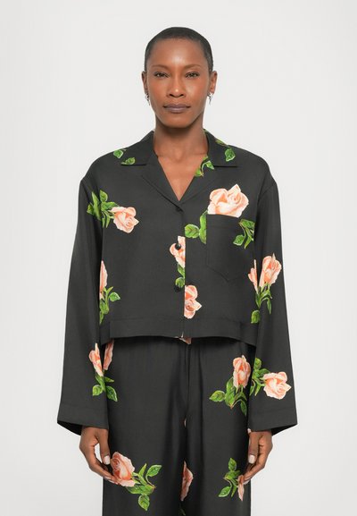 Veste noire cropped à manches longues, ornée d'un motif floral de roses rose clair et de feuilles vertes, avec une poche à l'avant.