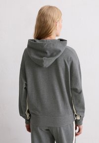 Szara bluza z kapturem o luźnym kroju. Posiada fakturowany materiał i kremowe boczne paski. Prosty design z ściągaczami na rękawach i u dołu.