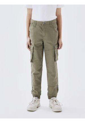 Child wearing olive green cargo pants with elastic cuffs and white sneakers, standing against a plain background.