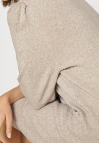 Beige stickad tröja med en mjuk textur, som har puffärmar och en avslappnad passform, vilket framhäver dess mysiga och varma utseende.