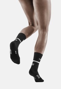 Schwarze Sportstrümpfe mit geripptem Schaft, weißen Streifen und strukturierten Mustern an der Seite, entworfen für Leistung und Unterstützung.