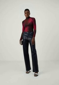 Tīрама, kas cieši pieguļ ķermenim, ar garām piedurknēm, pārejot no sarkanas uz melnu, apvienota ar augstām, tumši zilām džinsām un metāliskām augstpapēžu sandalēm.