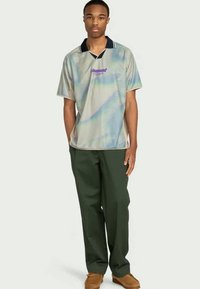Koszulka polo z krótkim rękawem, iryzująca, z granatowym kołnierzykiem i purpurowym logo, w połączeniu z zielonymi spodniami i brązowymi butami.