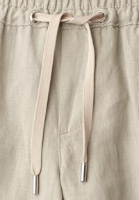 Pantalon en lin beige avec ceinture élastique et cordon noué avec embouts métalliques argentés et œillets.
