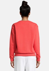 Sudadera coral con cuello redondo, mangas largas y puños acanalados. Textura suave con cintura ajustada. Sin logotipos ni patrones visibles.