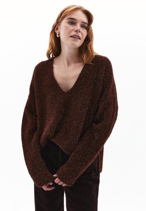 Brun tekstureret sweater med V-hals, lange ærmer og ribbede manchetter. Bæres over mørke bukser, der har en løs og afslappet pasform.