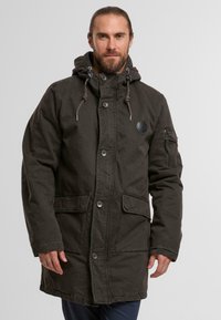Dunkelgrüne Parkajacke mit Kapuze, ausgestattet mit Druckknöpfen, zwei vorderen Taschen und einer mit Reißverschluss versehenen Ärmeltasche. Strapazierfähiger Stoff mit lässiger Passform.