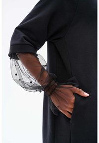 Schwarzer Pullover mit weicher Textur, der transparente schwarze Tüllärmel mit schwarzen Perlen und elastisch gerafften Manschetten aufweist.