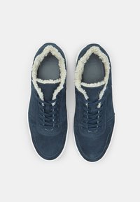 Jūras zilo zamšādu kedu ar greznu baltu mākslīgās pūkām oderi, plakaniem šņorēm, mīkstiem iekšējiem zoliņiem un baltajiem gumijas zoliem. Vienkāršs apaļais purngalu dizains.