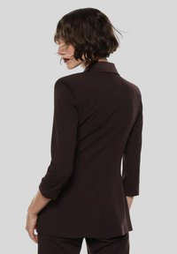 Blazer marrone su misura con una forma aderente, colletto a scollo a V e maniche tre quarti. Texture liscia con dettagli di cucitura sottili.
