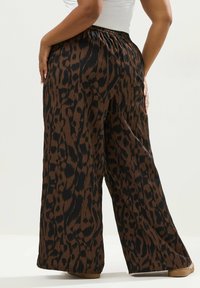 Vaatteet leveälahkeiset housut, joissa on ruskea ja musta leopardikuosi, teksturoitu kangas ja elastinen vyötärö, näkyy takaa.