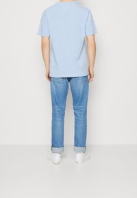 Ljusblå bomull t-shirt med korta ärmar, kombinerad med ljusblå jeans och vita sneakers, som visar en avslappnad passform och uppvikta fållar.