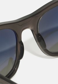 Ochelari de soare negri cu un cadru gros, având lentile în degrade închise și o textură netedă. Design curbat notabil la punte.