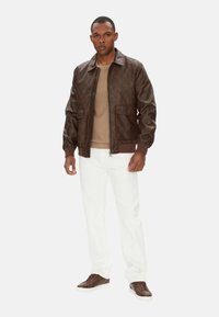 Giubbotto bomber in pelle marrone con un sottile motivo in rilievo, abbinato a un maglione beige, pantaloni bianchi e sneakers marroni.