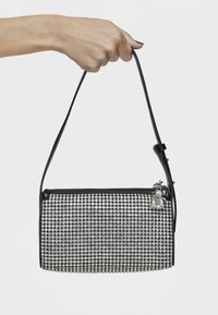 Czarna torebka z ozdobami z cyrkonii, prostokątny kształt, cienki pasek na ramię i mały metalowy szczegół w postaci zawieszki.