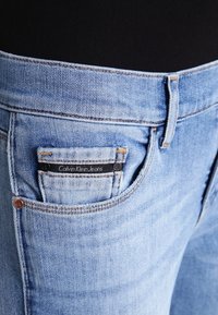 Ljust blå denimjeans med en klassisk design, som har en bakficketikett "Calvin Klein Jeans" och kontrasterande orange sömmar.