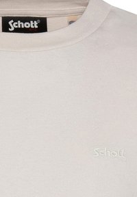 T-shirt in cotone grigio chiaro con collo a costine. Presenta un logo "Schott" ricamato sul petto. Texture liscia, design minimalista.