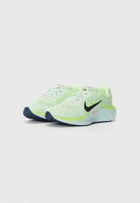 Svijetlozeleni tenisice za trčanje s mrežastim gornjim dijelom, crnim Nike logotipom i plavim gumastim potplatom. Imaju udoban potplat i dizajn s vezicama.